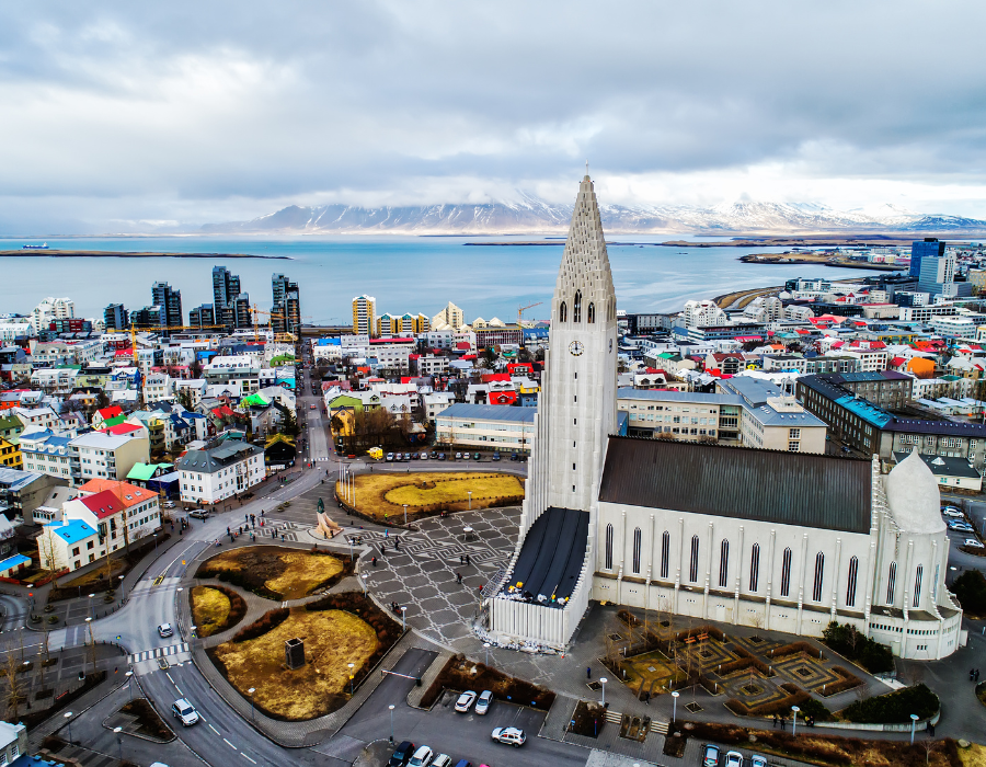 Widok z boku na kościół Hallgrímskirkja w Reykjaviku na Islandii oraz na plac przed kościołem i domy. W tle góry.